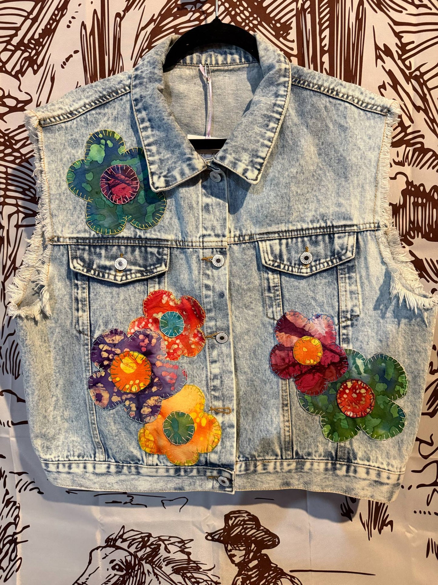 Front View: Light wash denim vest with multicolor retro floral appliqués and frayed sleeves, XXL