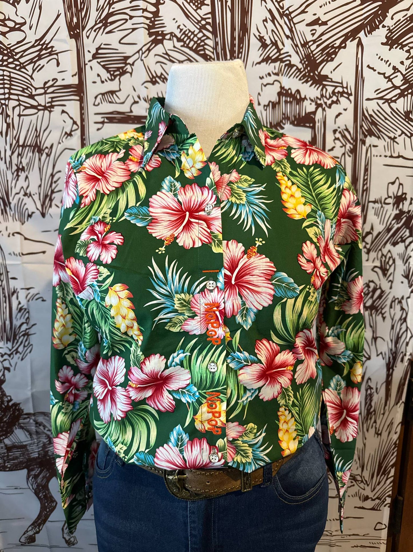 A vibrant green button-up shirt with pink hibiscus and yellow pineapple print, displayed on a mannequin with a leather belt and denim jeans.