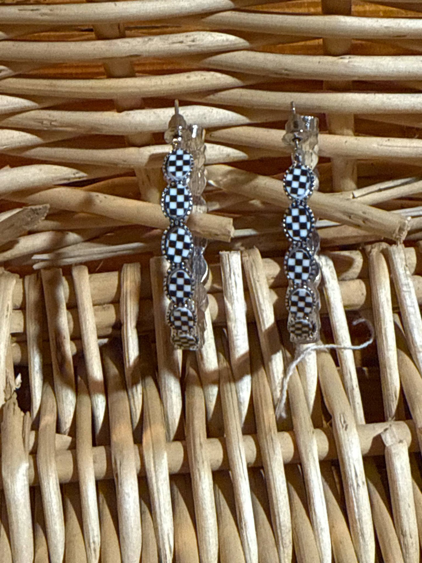 Pair of silver hoop earrings featuring black-and-white checkerboard oval accents with scalloped edge detail, displayed on a wicker background.