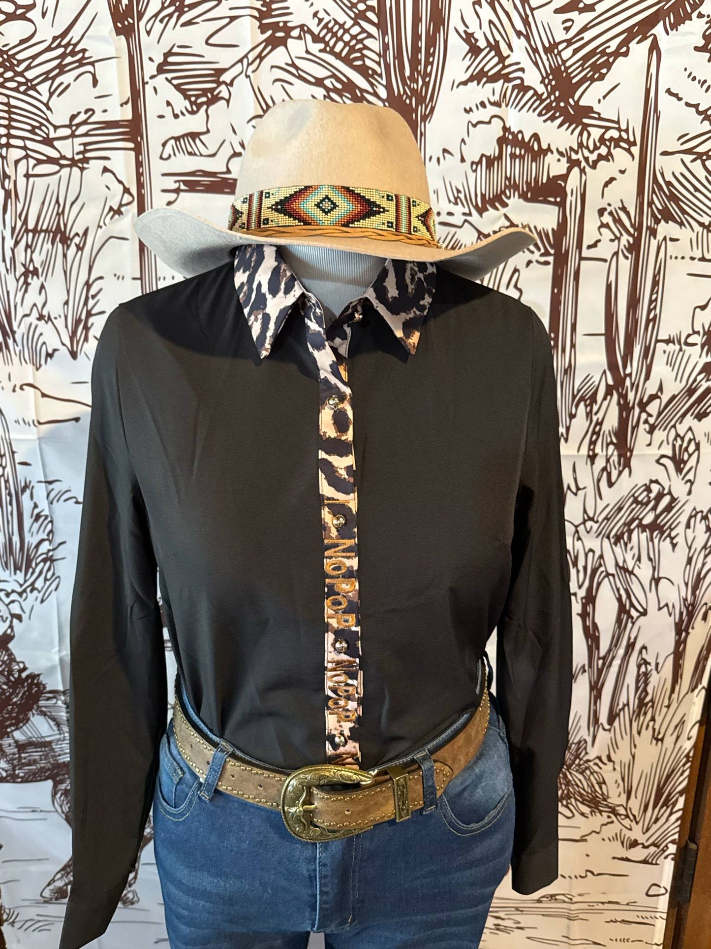 Black NoPop button-up shirt with a leopard print collar and button placket, shown on a mannequin styled with a tooled leather belt, denim jeans, and a cream-colored hat with a tribal beaded band.