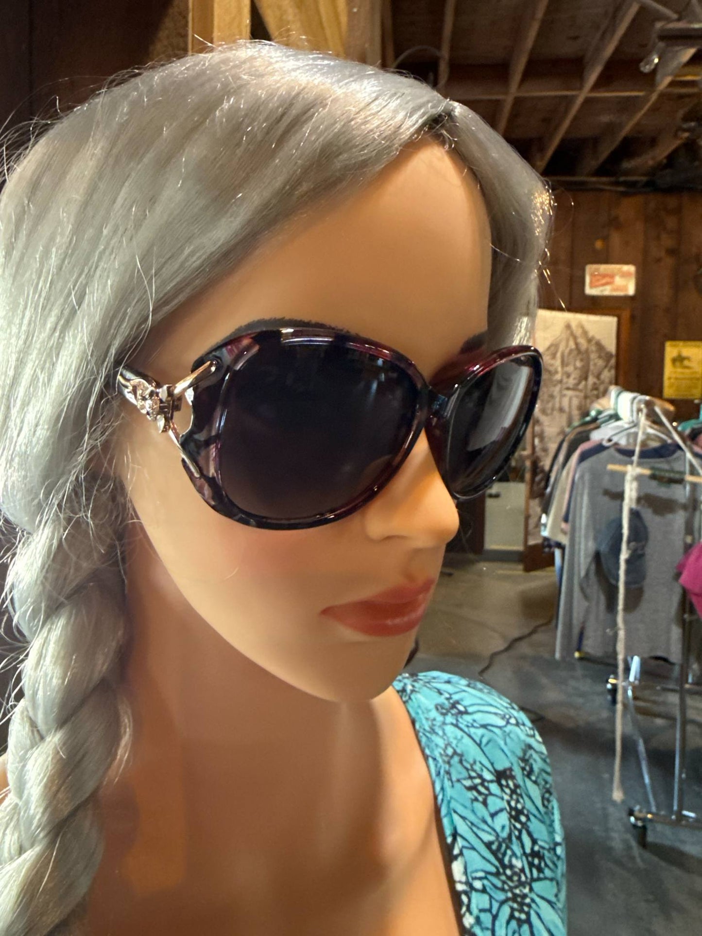 Mannequin with braided hair wearing oversized polarized sunglasses with dark lenses and a touch of tortoise shell on the frame, featuring silver western-style detailing on the sides.