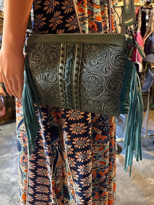 Tooled leather crossbody purse in sage green with floral embossing, braided center detail, stud accents, and fringe on both sides.