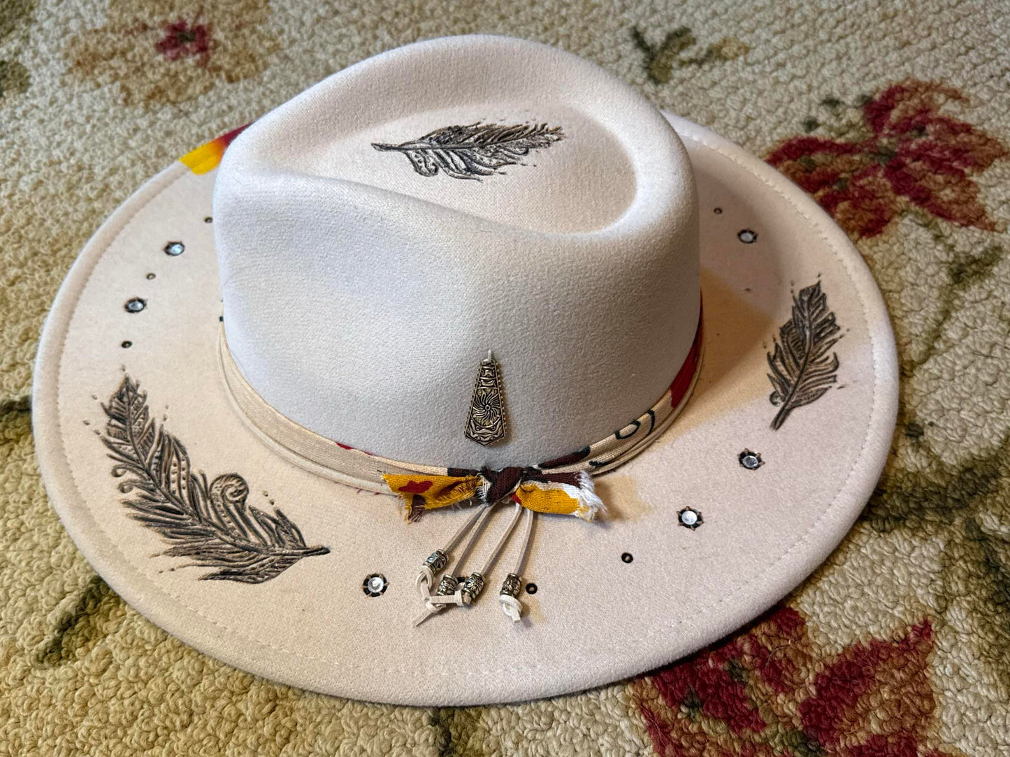 Cream-colored fedora with hand-burned feather designs, crystal details, and a mixed-fabric band from the Amira Collection.