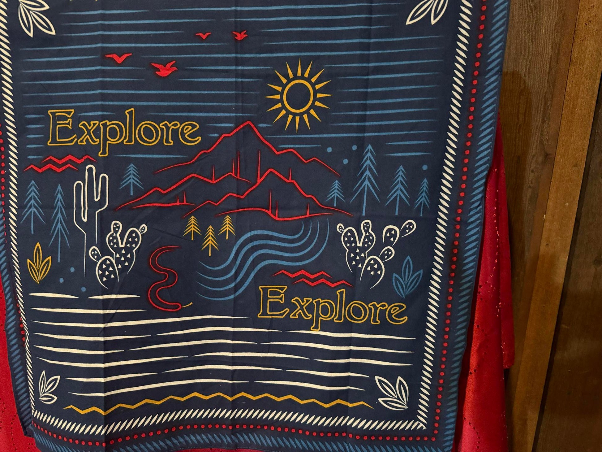 Blue cowboy scarf with red, yellow, and white illustrations of a desert landscape and “Explore” text.