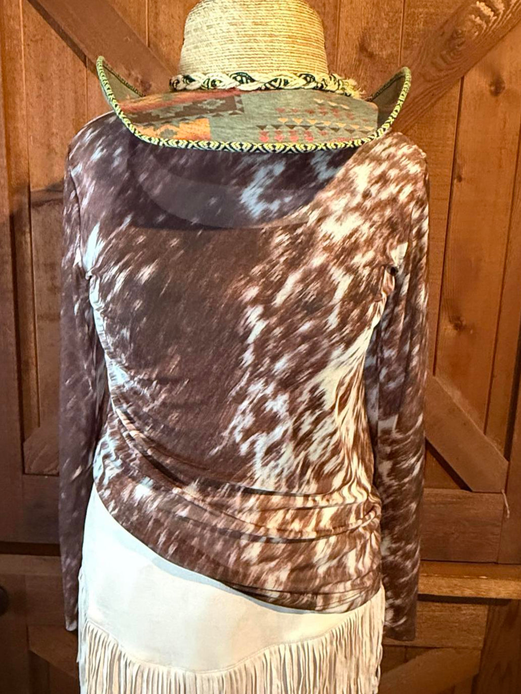 Brown and white cowhide-print mesh long-sleeve top displayed with a suede fringe skort and western hat.
