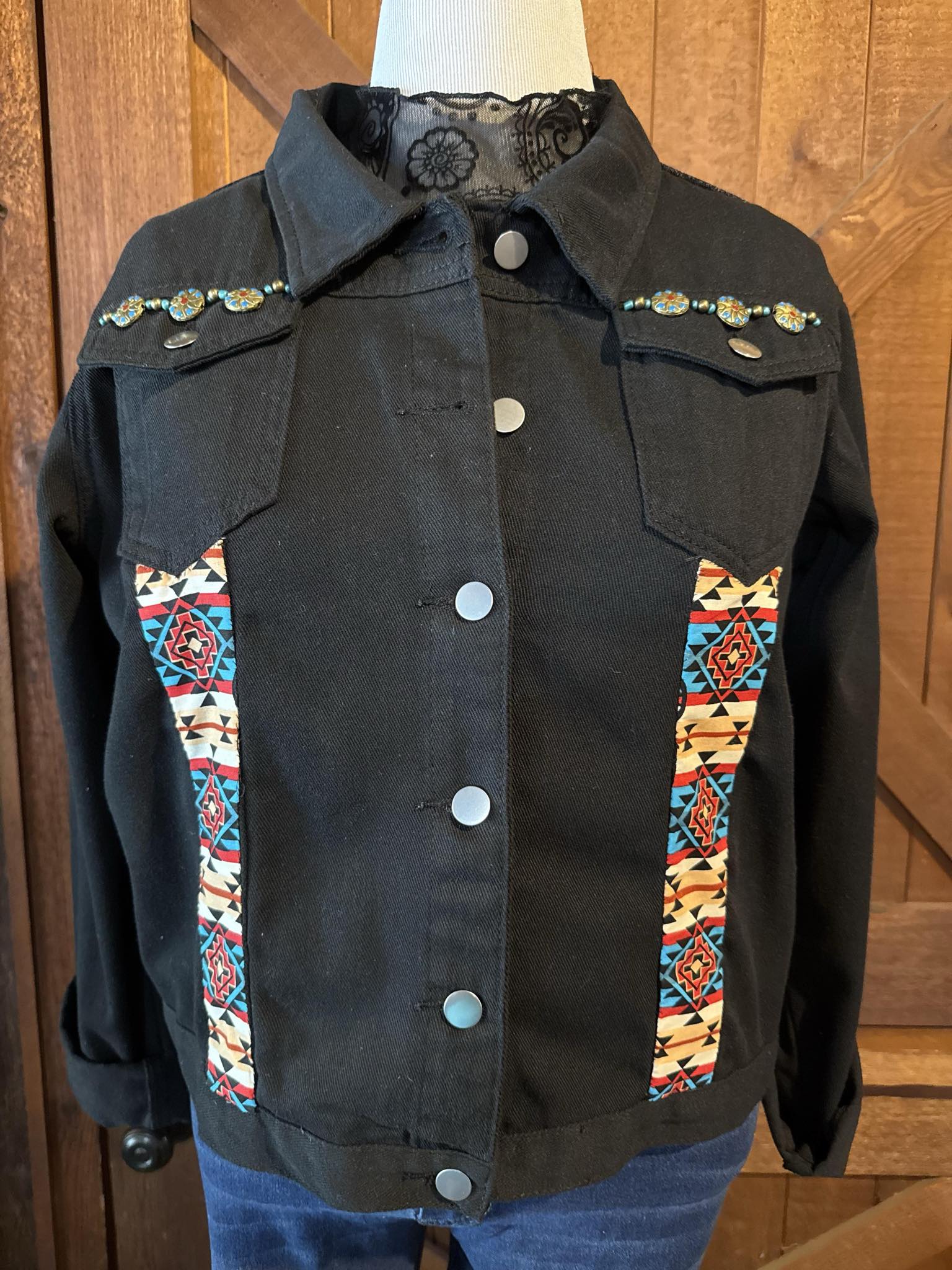 Hand-embellished black denim jacket with vibrant Aztec print panels, turquoise beaded accents, and silver snap buttons. One-of-a-kind design in size XXL.