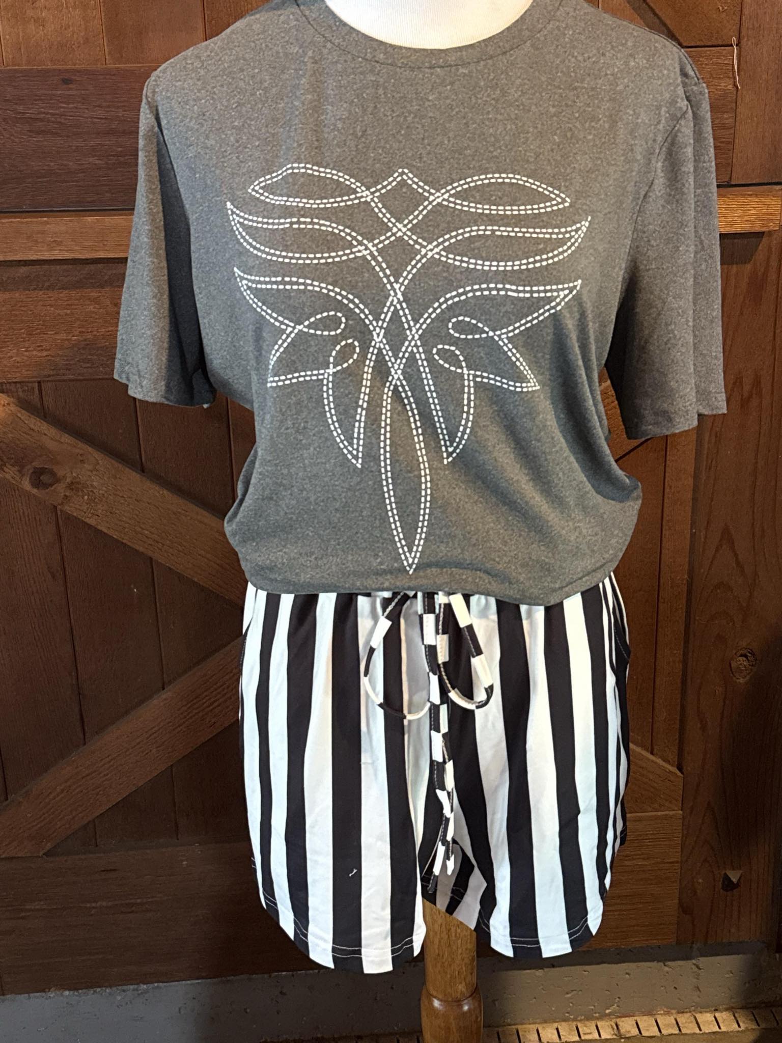 Heather gray short sleeve t-shirt featuring a white stitched western boot-inspired graphic design across the chest, styled with black and white striped drawstring shorts on a mannequin.