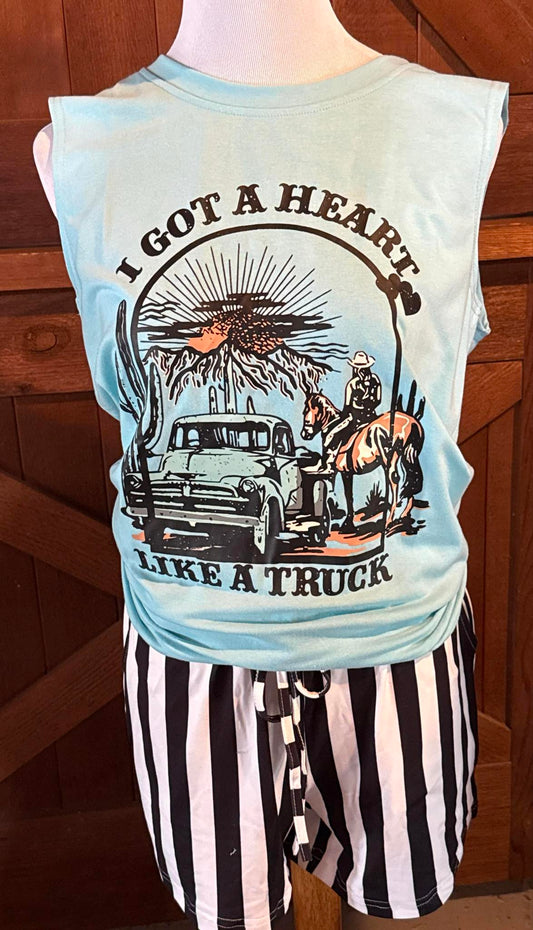 Light blue sleeveless tank top with a western graphic featuring a vintage pickup truck, a cowboy with a horse, a desert scene, and the phrase “I Got a Heart Like a Truck,” displayed on a mannequin with black and white striped shorts.

