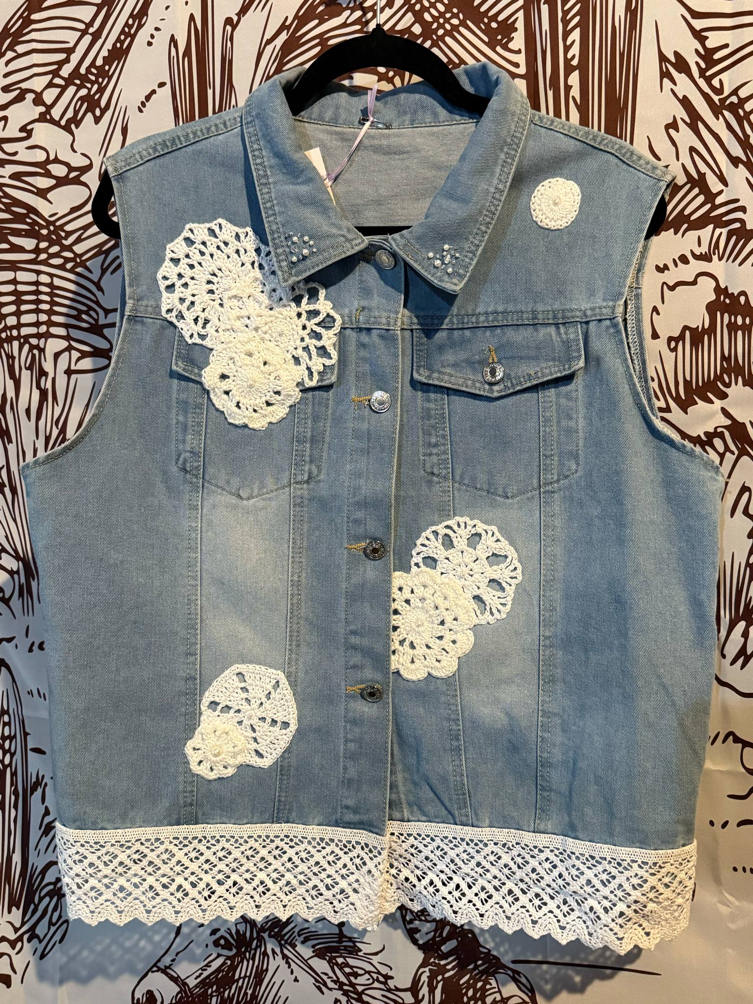 Front View: Light denim vest with white crocheted doilies and vintage lace trim along the hem, size XXL