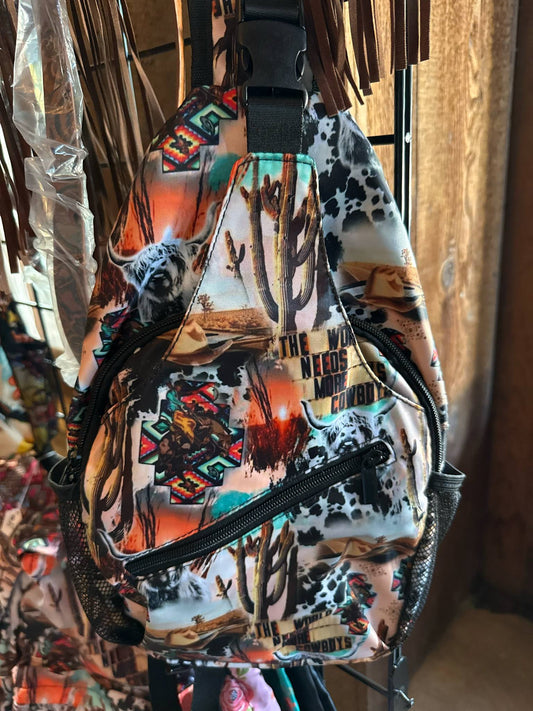 Western-themed sling backpack featuring cactus, cowhide, and cowboy prints with the phrase "The World Needs More Cowboys" in bold lettering.