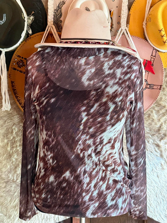 Brown and white cow-print mesh long-sleeve top displayed on a mannequin with a cream western hat, styled against a rustic background.