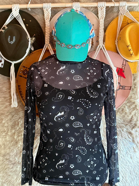 Black long-sleeve mesh top with white western paisley designs displayed on a mannequin wearing a turquoise cap and silver concho band.