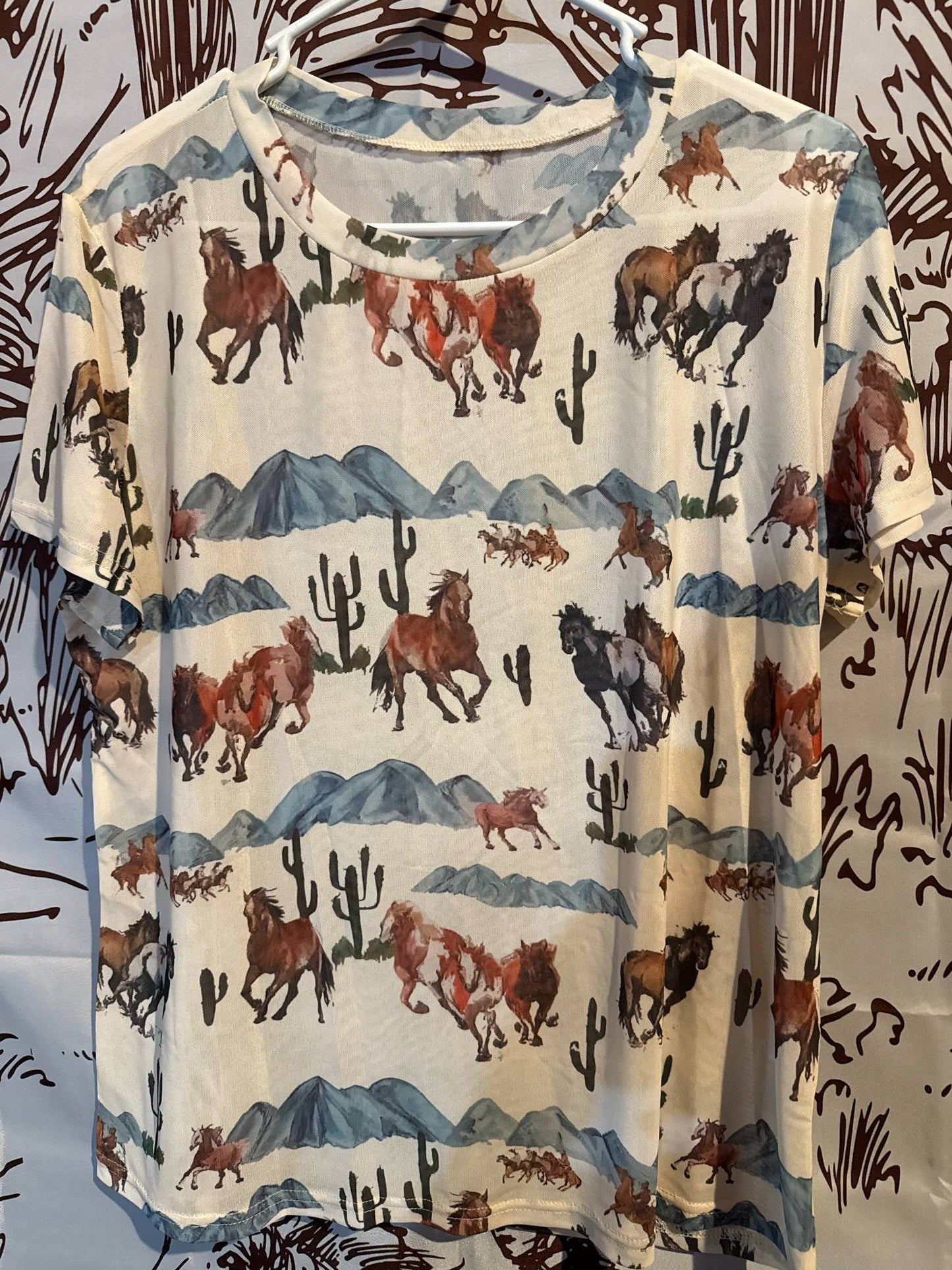 Short-sleeved cream mesh shirt featuring a watercolor-style desert scene with galloping horses, mountains, and cacti.