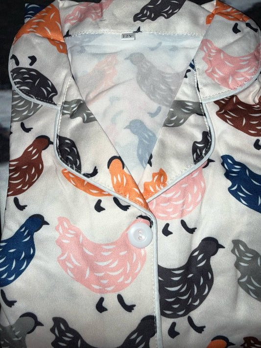 Kids pajama set with colorful chicken print in pink, orange, blue, gray, and black on a cream background